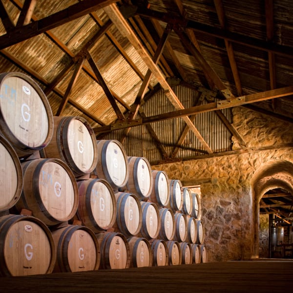 Holzfässer ordentlich in Reihen gestapelt in einem rustikalen Weinkeller mit Steinwänden und einem Wellblechdach im Valle de Guadalupe, Mexiko.