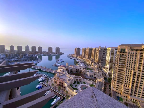 Ein Panorama von The Pearl Doha mit luxuriösen Gebäuden, einem Yachthafen und klarem blauem Himmel bei Sonnenuntergang.