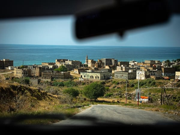 View through a car windshield of the coastal fishing village of Hawf in Yemen with traditional buildings near the sea.