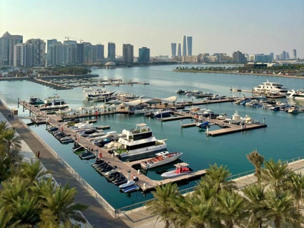 Yachthafen in Lusail mit Anlegestellen voller verschiedener Boote und Yachten, vor einer Kulisse moderner Hochhäuser unter klarem Himmel.