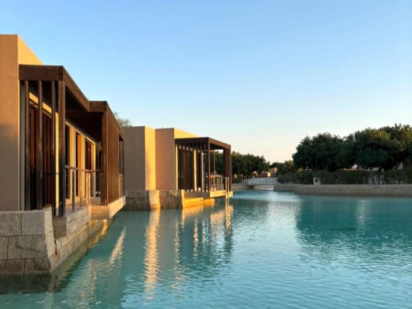 Moderne Resorts mit großen Glasfenstern, die sich in einer ruhigen türkisfarbenen Lagune bei Sonnenuntergang spiegeln.