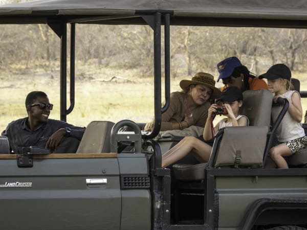 A group of tourists, including children and an adult woman, taking pictures and enjoying a safari ride in a Land Cruiser in Botswana.