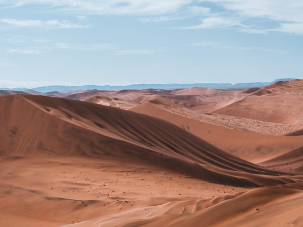 Weite rote Sanddünen in einer Wüstenlandschaft unter einem teils bewölkten Himmel in Namibia.