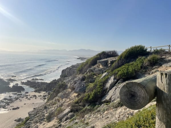 Beachside rocky coastline with sandy beach and ocean waves under a clear blue sky.