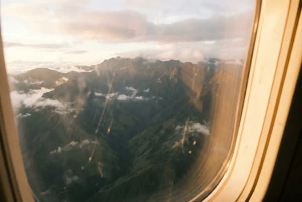 Blick auf grüne Anden-Berglandschaft mit Wolken bei Sonnenuntergang durch ein Flugzeugfenster.
