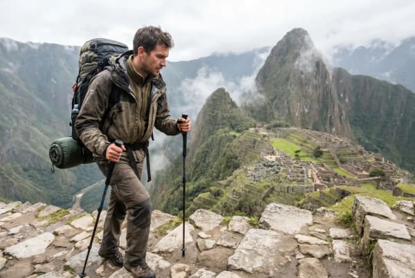 Ein Mann wandert mit Wanderstöcken und großem Rucksack bei Machu Picchu, umgeben von nebligen Bergen und antiken Steinruinen.