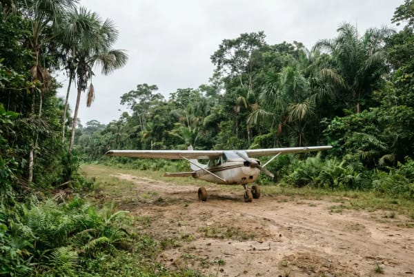 Ein kleines einmotoriges Flugzeug steht auf einer unbefestigten Landepiste, umgeben von dichtem tropischem Regenwald.