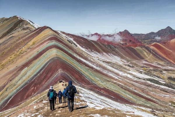Wanderer gehen die farbenfrohen, gestreiften Hänge des Rainbow Mountain in Peru bei klarem Himmel hinunter.