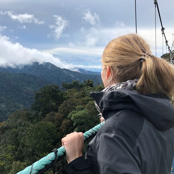 Frau steht auf einer Hängebrücke im Nyungwe Wald und blickt über den Regenwald