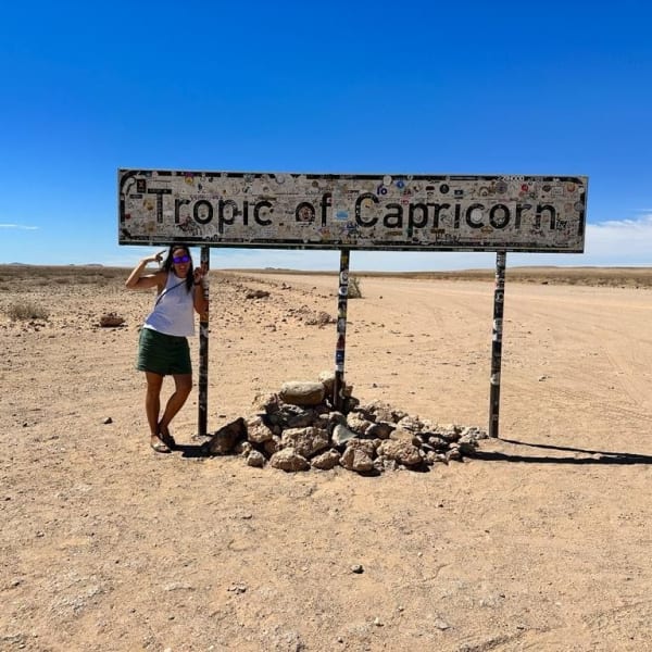Frau steht unter dem Schild "Tropic of Capricorn" in Wüstenlandschaft