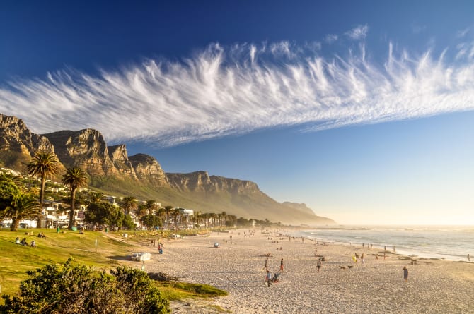 Strand von Camps Bay mit Bergen im Hintergrund und Menschen im Sand