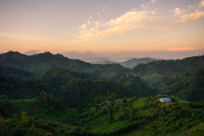 Sonnenaufgang über grünen Hügeln im Bwindi-Nationalpark, Uganda, mit einem kleinen Haus auf einem Hügel.