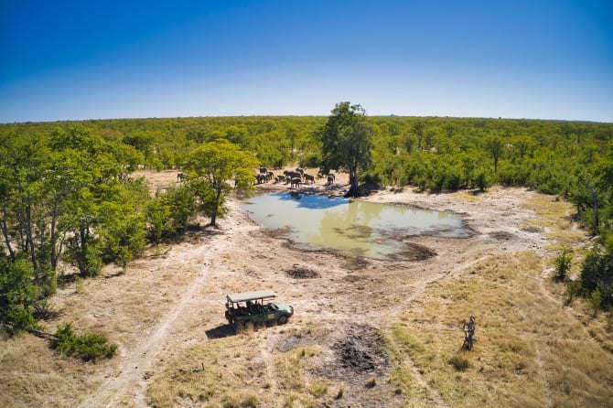 Safarifahrzeug an einem Wasserloch im Hwange Nationalpark mit Elefanten