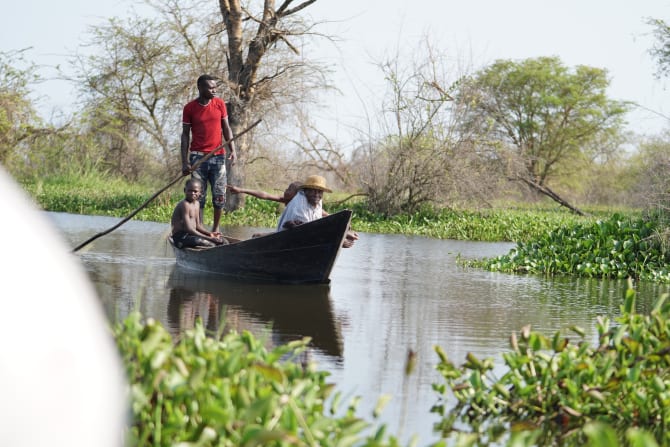 Drei Männer sitzen in einem kleinen Boot und fahren über einen flachen See