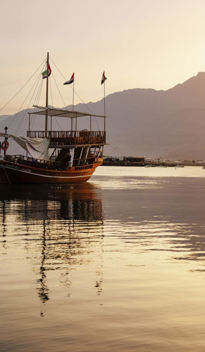 A traditional boat floating on calm waters during sunset with mountains in the background.