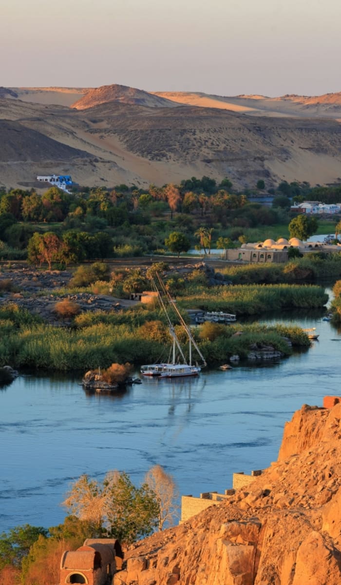 Eine landschaftliche Aussicht auf den Nil mit Booten, grünen Ufern und Wüstenhügeln in Ägypten.