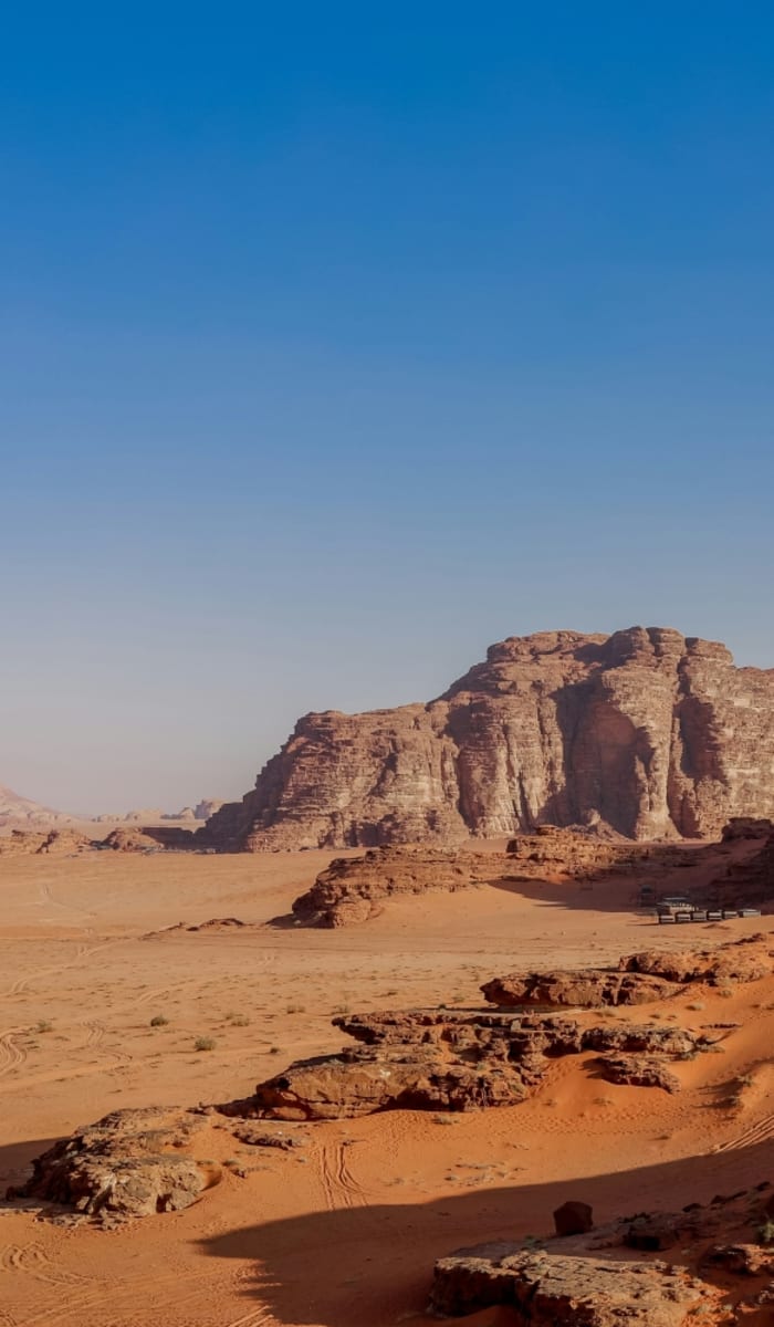 Weite Wüstenlandschaft in Wadi Rum mit Felsformationen unter klarem blauen Himmel.