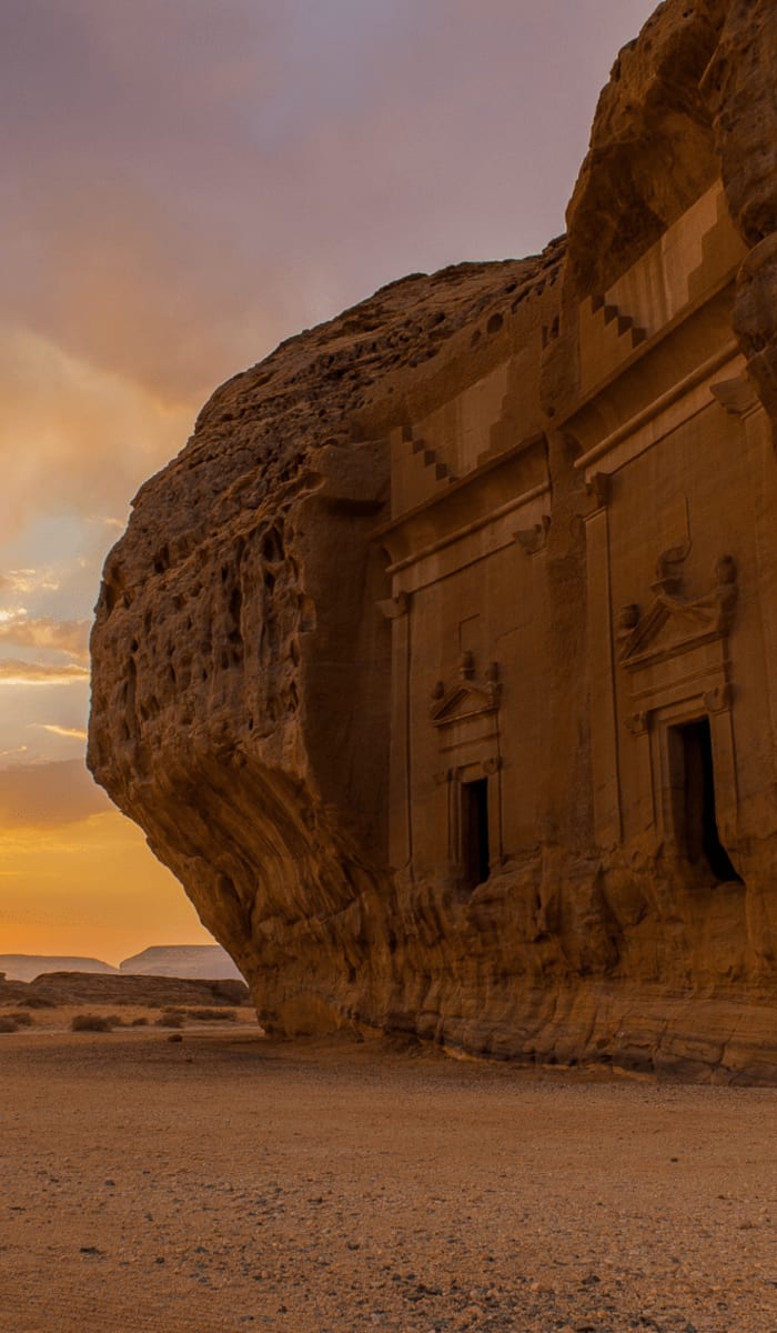 Antike in eine Felswand gearbeitete Bauwerke mit Sonnenuntergang im Hintergrund in Hegra, AlUla, Saudi-Arabien.