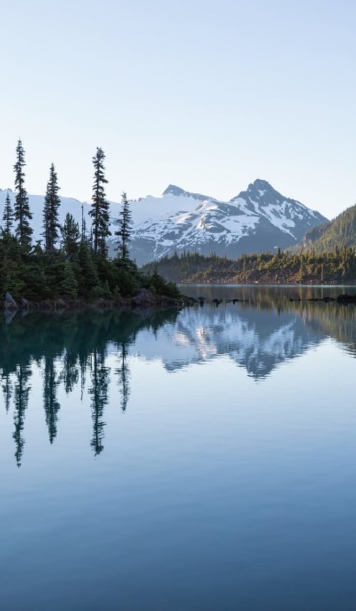 Ein Panoramablick auf Berge, Kiefern und einen ruhigen See, der die Landschaft in Whistler, Kanada, widerspiegelt.
