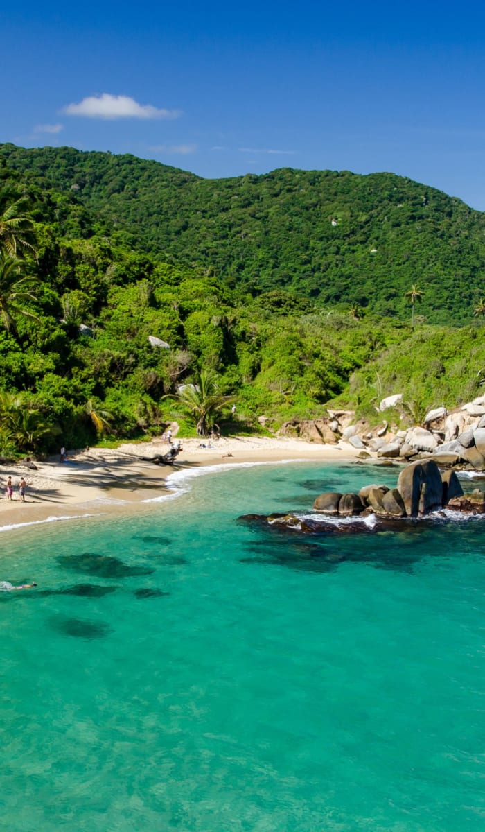 Tropischer Strand mit üppigen grünen Bergen und Palmen entlang der Küste in Kolumbien.