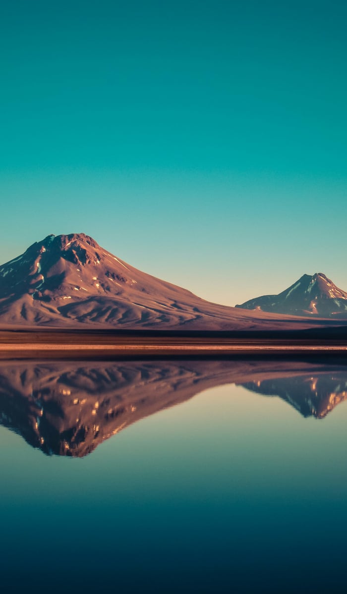 Eine ruhige Landschaft mit vulkanischen Bergen, die in einem stillen See im Morgengrauen in der Atacama-Wüste gespiegelt werden.