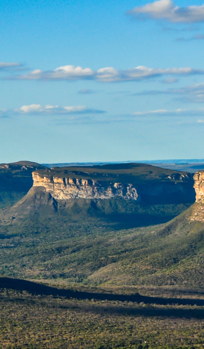A panoramic view of the cliffs and canyon in the Chapada Diamantina, Brazil, with a partly cloudy sky overhead.