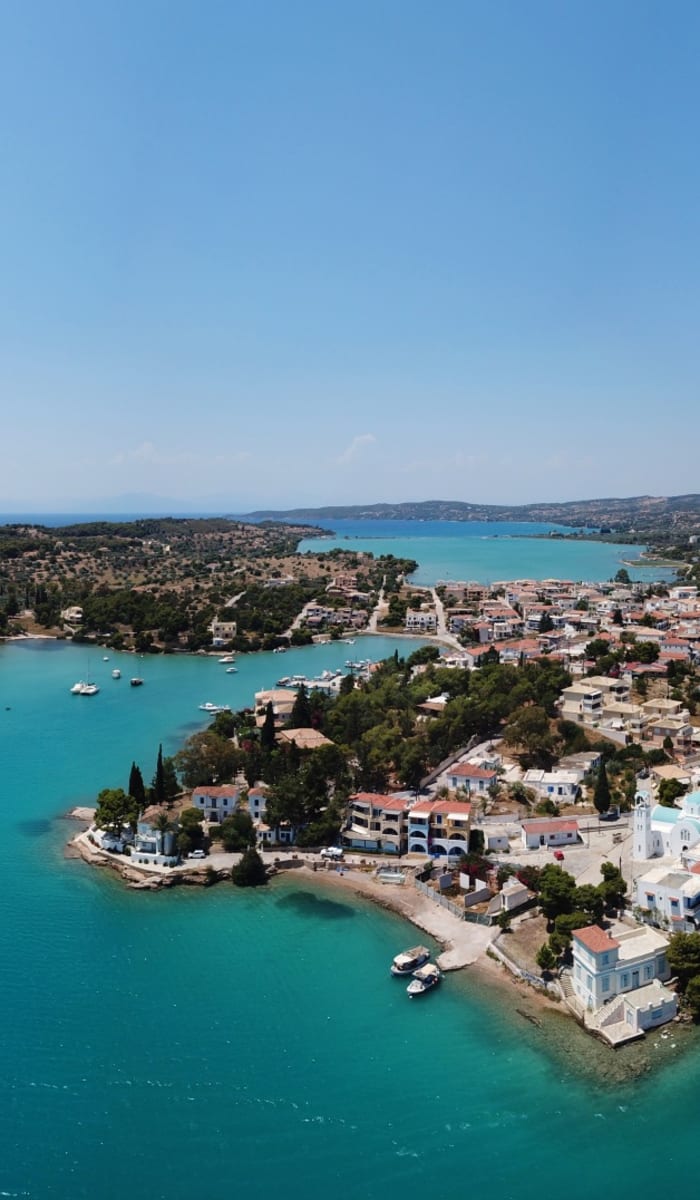 Luftaufnahme von Porto Heli mit Blick auf den Hafen, die umliegenden Gebäude und das türkisfarbene Wasser.