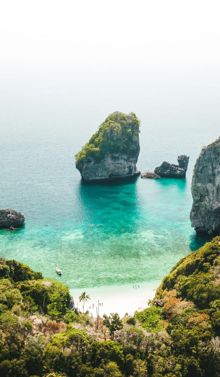 A secluded beach surrounded by steep, lush green cliffs and emerald waters in Thailand