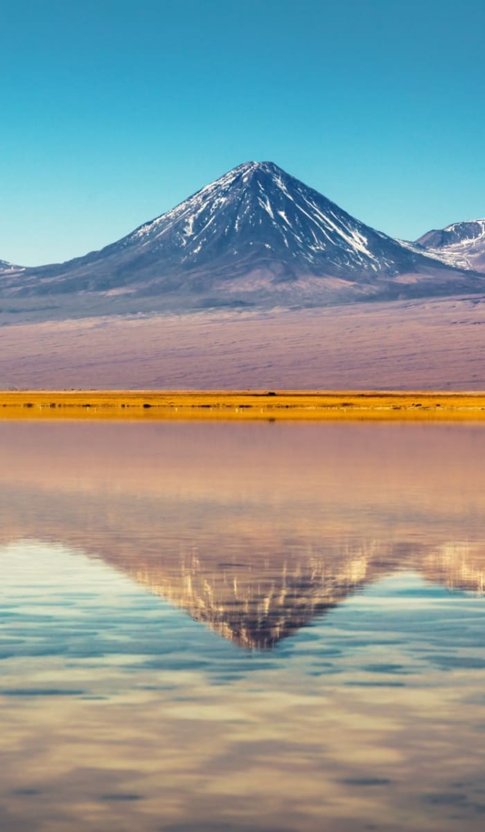 Ein Panoramablick auf die Atacama-Wüste mit schneebedeckten Bergen, die sich im See spiegeln.