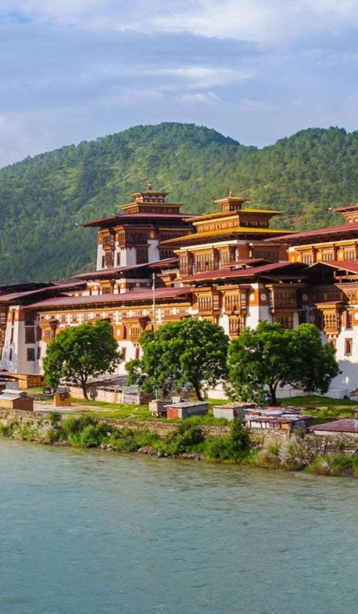 Ein traditioneller bhutanischer Kloster oder Palast in der Nähe eines Flusses mit grünen Bergen im Hintergrund.