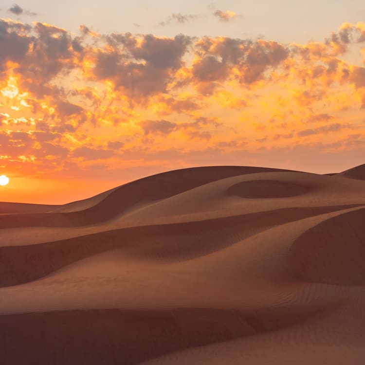 Sunset over the sand dunes of Wahiba Sands in Oman with colorful clouds in the sky.