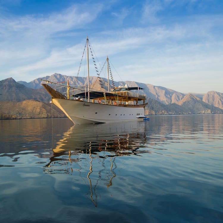 Ein traditionelles Holzboot, das auf ruhigem Wasser treibt, mit Berglandschaft im Hintergrund.
