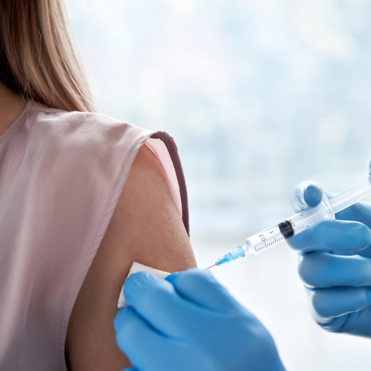 A person receiving a vaccine injection in their upper arm by a healthcare worker wearing blue gloves.