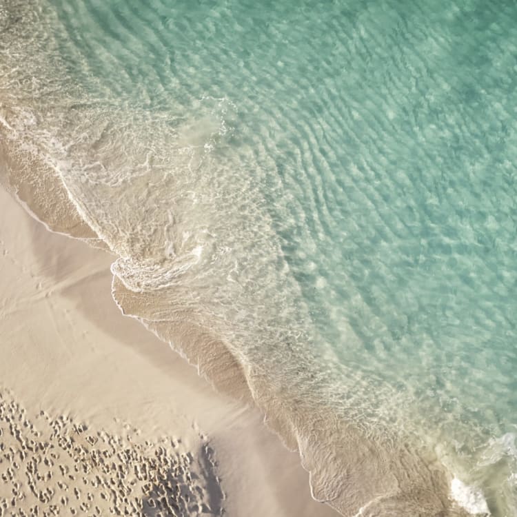 Aerial view of a beach with clear turquoise water gently lapping onto soft white sand.