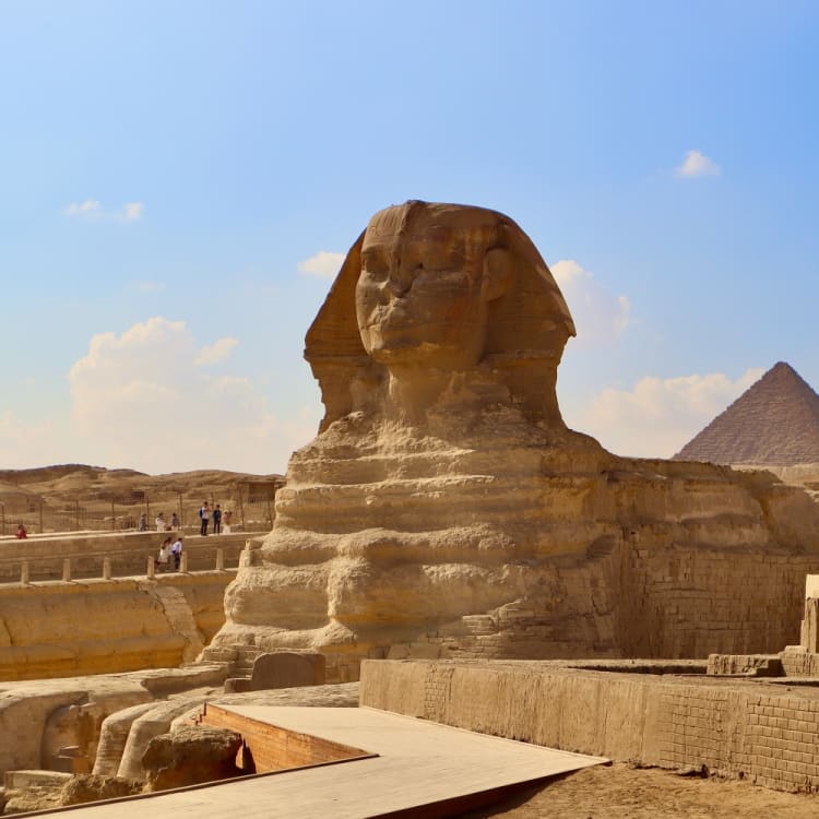 The Great Sphinx of Giza with the Pyramid of Khafre visible in the background under a bright blue sky with some clouds.