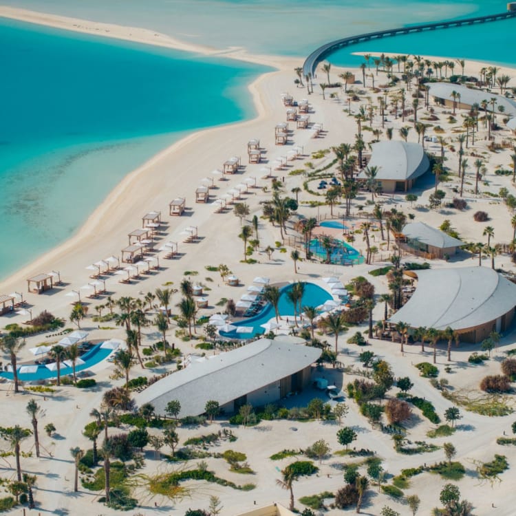 Luftaufnahme eines luxuriösen Strandresorts mit weißen Sandstränden, Swimmingpools und zahlreichen Palmen.