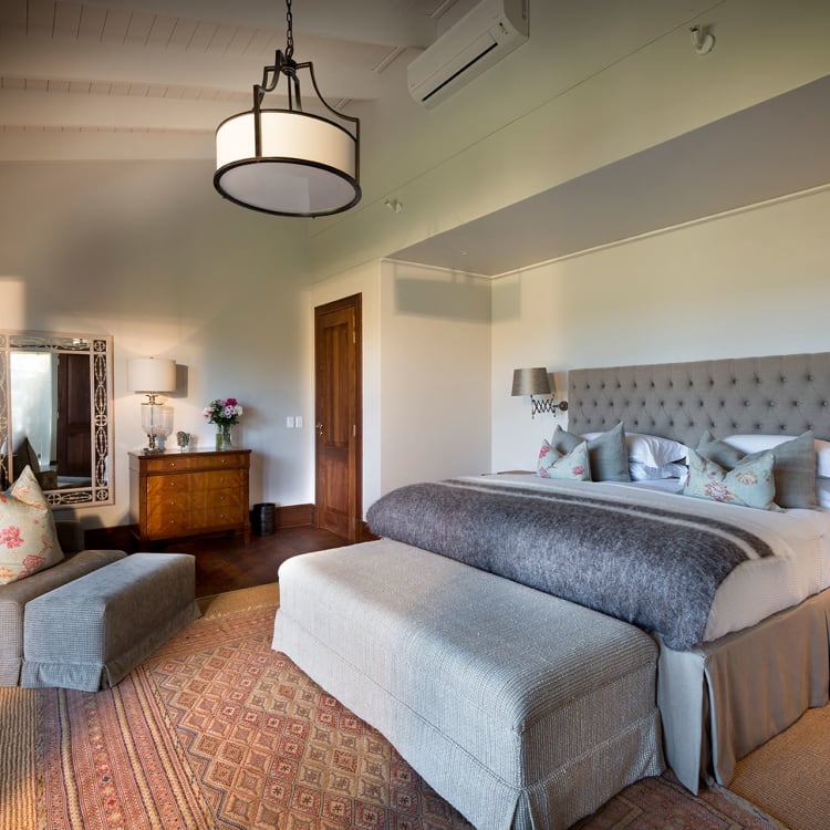 Ein geräumiges, luxuriöses Schlafzimmer in einem Safari-Lodge-Haus mit eleganter, moderner Einrichtung. Das Zimmer verfügt über ein großes, komfortables Kingsize-Bett mit einem gepolsterten Kopfteil und dekorativen Kissen.