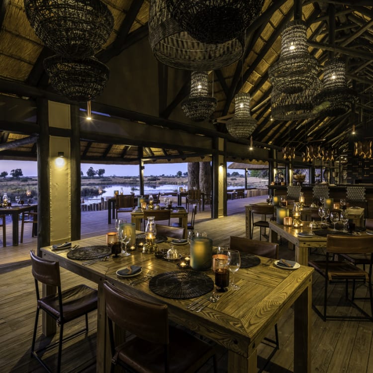 Elegantes Restaurant mit offener Holzterrasse, stilvollen Hängelampen und einem Blick auf die umliegende Landschaft bei Dämmerung.