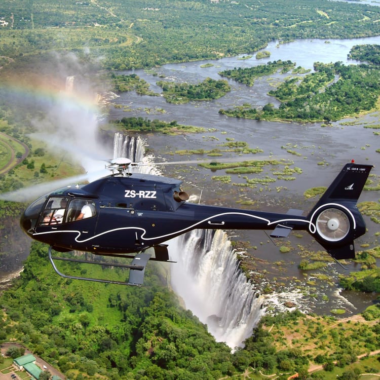 Ein Hubschrauber fliegt über die Victoriafälle mit einem Regenbogen in der Nähe des Wasserfalls