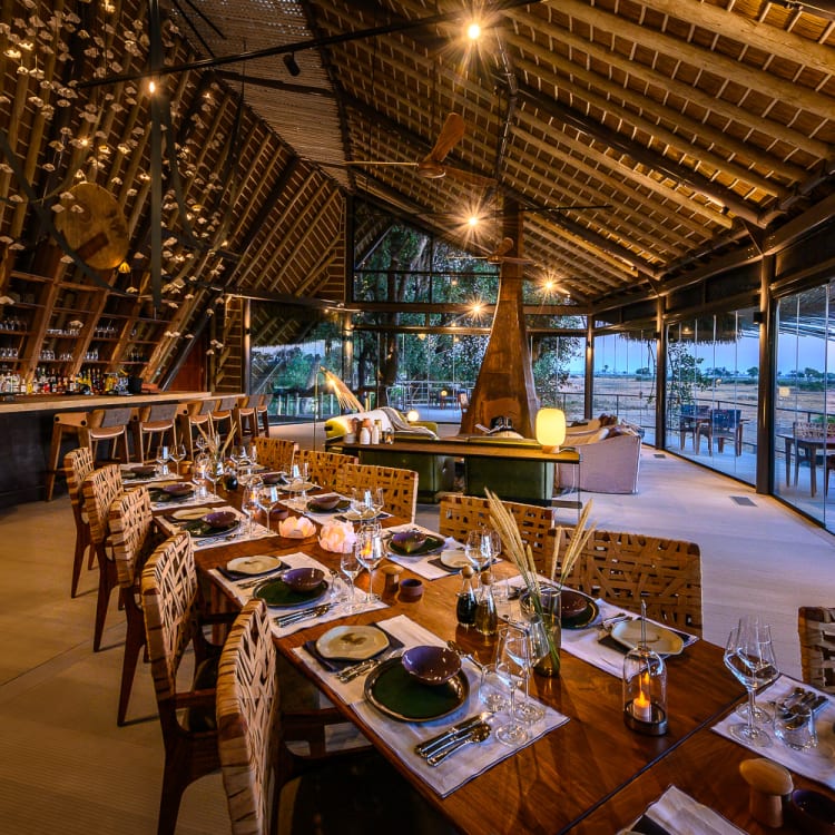 Stimmungsvolles Speisezimmer mit elegant gedecktem Tisch und einer offenen Bar, eingerahmt von einem kunstvoll gestalteten, hohen Dach aus natürlichen Materialien, das einen weiten Blick auf die umliegende Landschaft bietet.