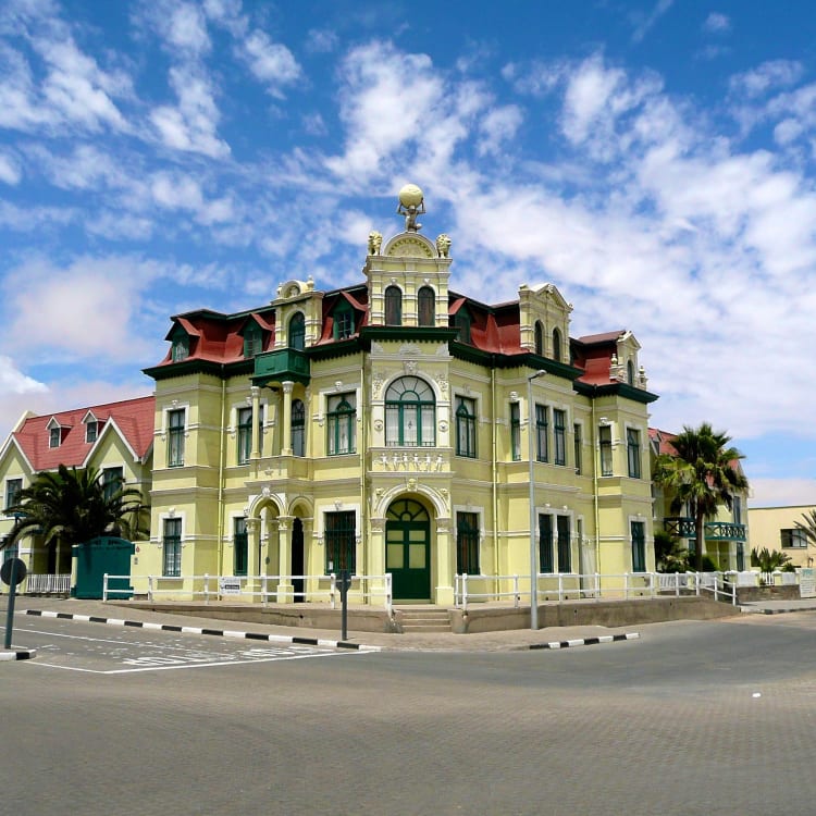 A historic ornate building with a green facade and red roof in Swakopmund, Namibia, under a partly cloudy sky.
