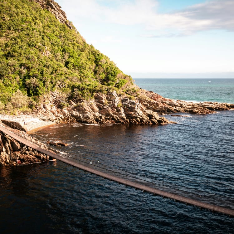 A scenic view of the coast with a rocky shoreline, green hillside, and an ocean extending to the horizon with a small boat in the distance.