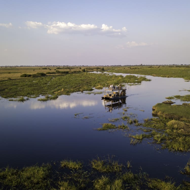 Ein Boot fährt gemächlich durch weitläufige Wasserwege, umgeben von üppigem Grün und weitem Himmel.