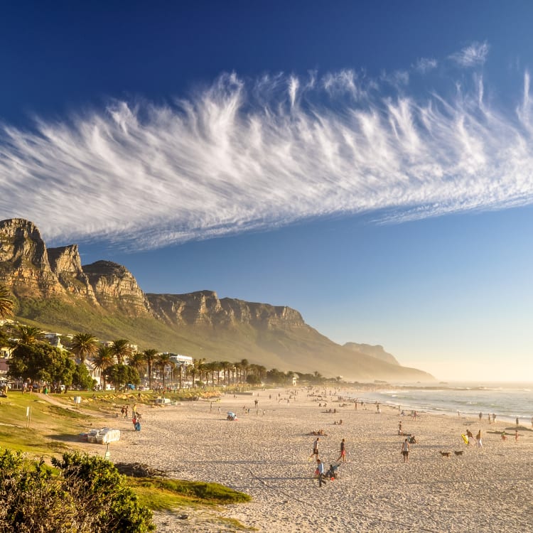 Strand von Camps Bay mit Bergen im Hintergrund und Menschen im Sand