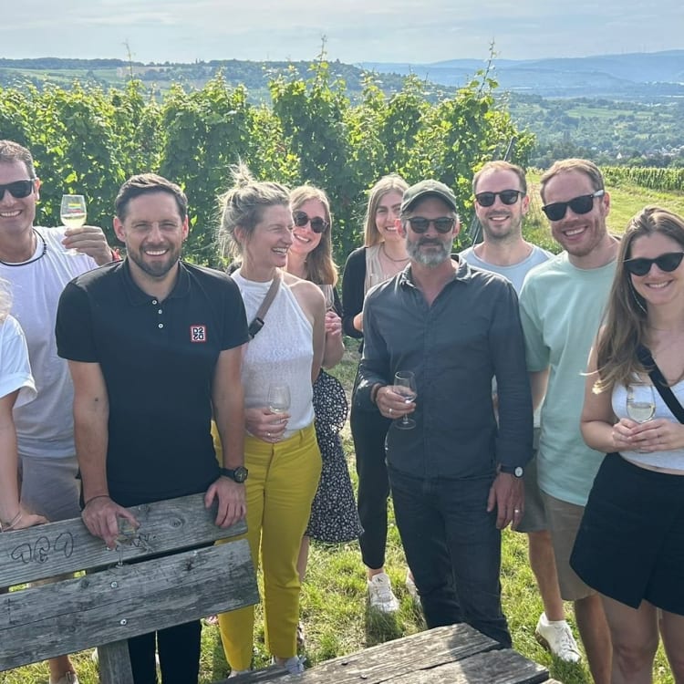 Eine Gruppe von Menschen, die ein Treffen in einem Weinberg mit malerischer Landschaft im Hintergrund genießen.