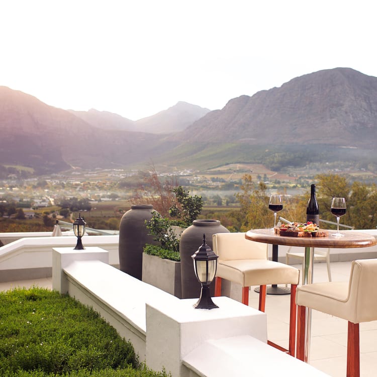 A terrace with a table set for drinks overlooking a valley with mountains in the background.