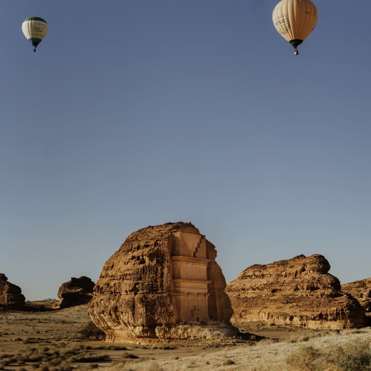 Zwei Heißluftballons schweben über einer felsigen Wüstenlandschaft mit großen Felsformationen.