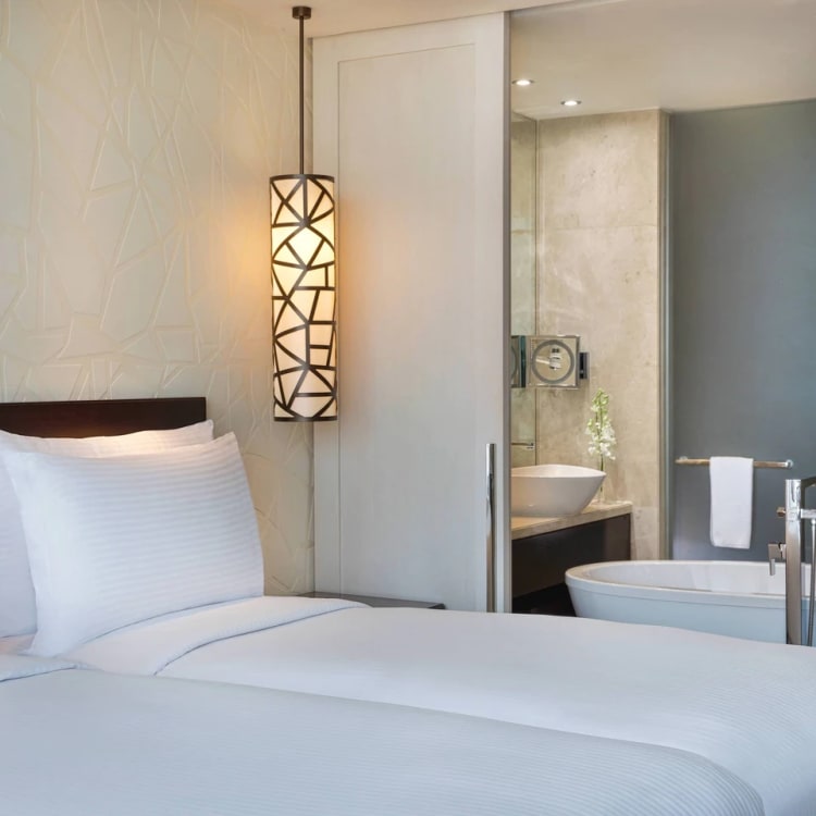 Part of a hotel room overlooking parts of a bed into a big bathroom with a bathtub