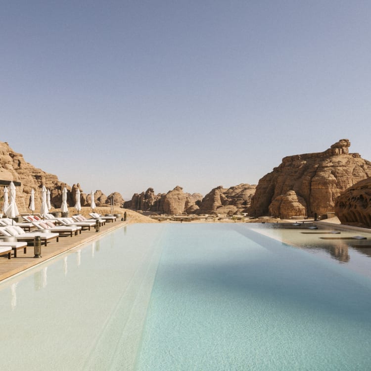 A big rectangular infinity pool with a view overlooking the desert and rock shapes and lounge chairs on the left