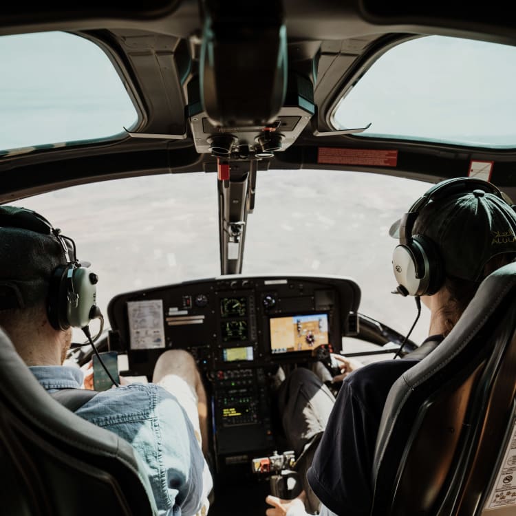 Zwei Piloten in einem Hubschrauber-Cockpit fliegen während des Tages über eine Landschaft.